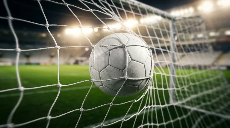 Red de portería de fútbol vista desde dentro con un balón entrando y césped verde de estadio profesional